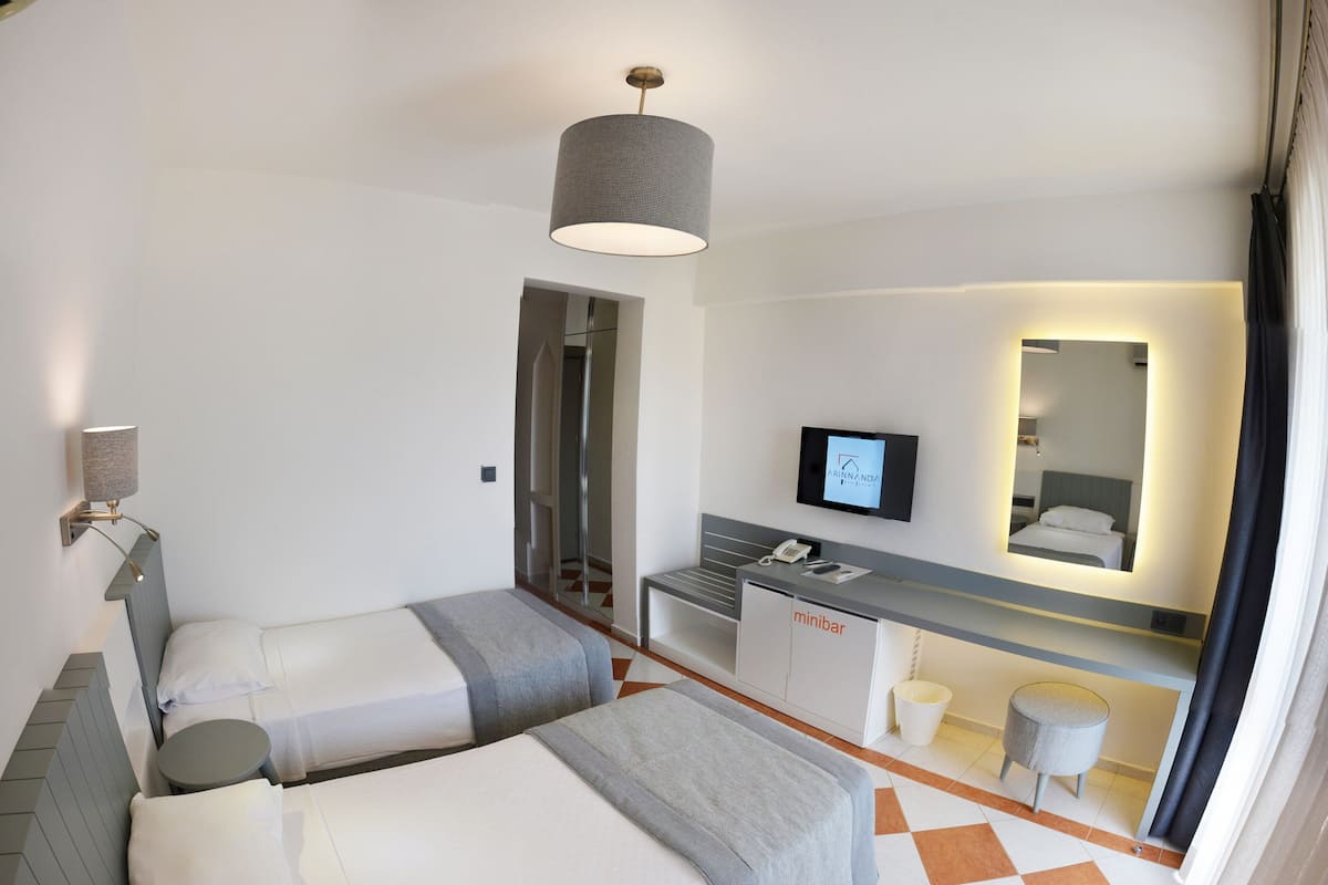 A hotel room with two beds, a desk with a computer, a mirror, and a minibar.