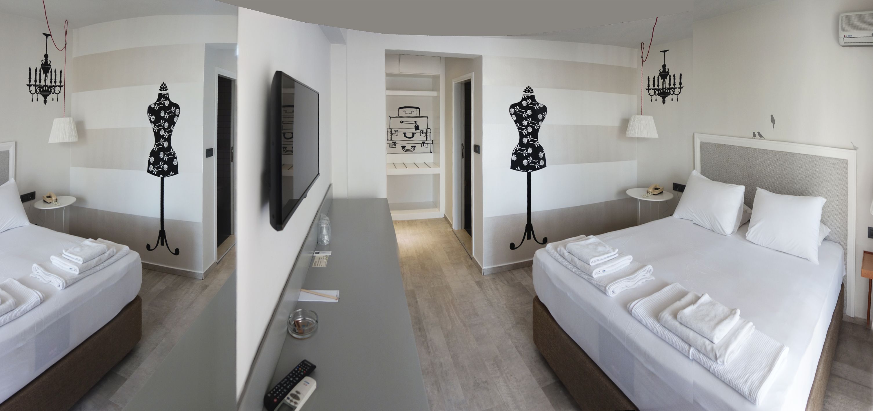A hotel room with two beds, a desk with a flat-screen TV, a minibar, and a wall-mounted TV.