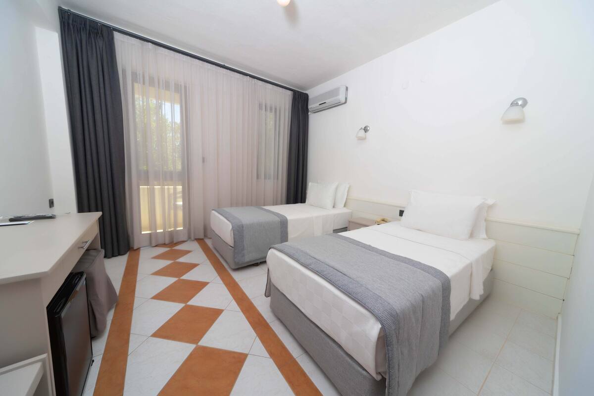 A hotel room with two beds, a desk, and a window with curtains.