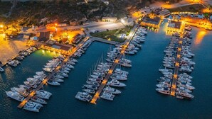 Vista aérea de un puerto deportivo con varios muelles y barcos, rodeado de edificios y una carretera.
