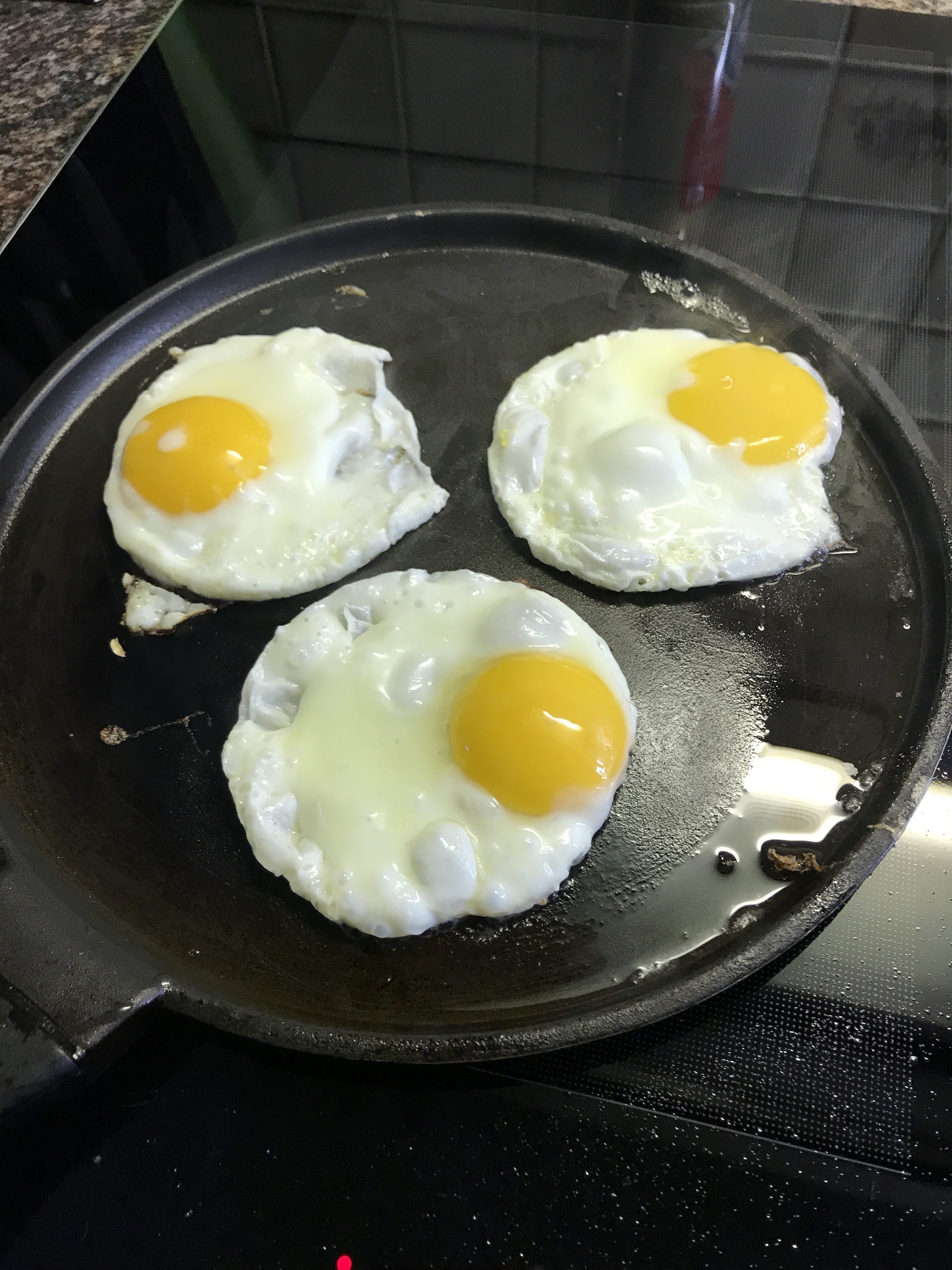 Tre stekt ägg, stekta med äggulan uppåt, i en svart stekpanna.