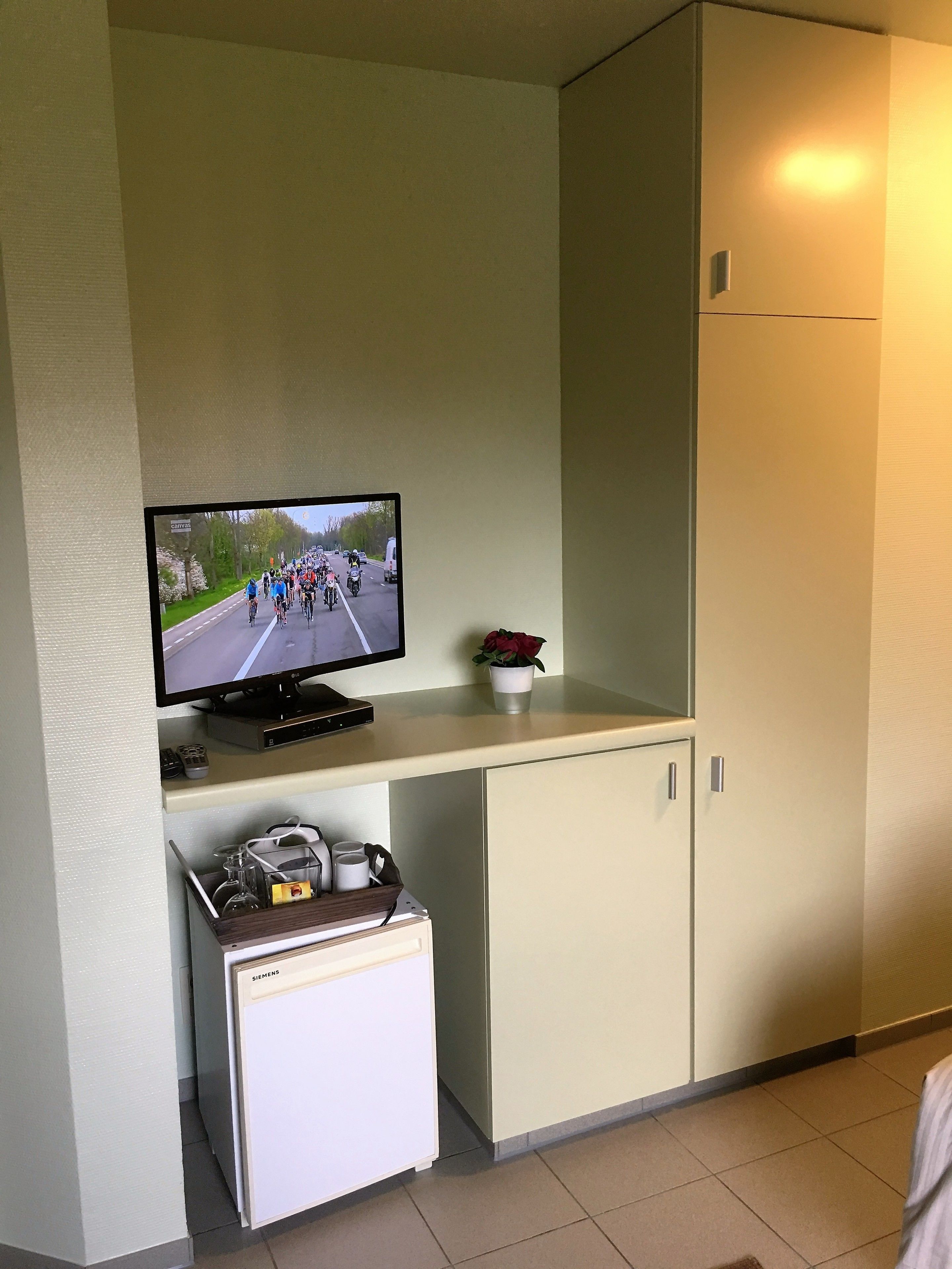 A room with a television mounted on a wall, a small refrigerator, and a cabinet.