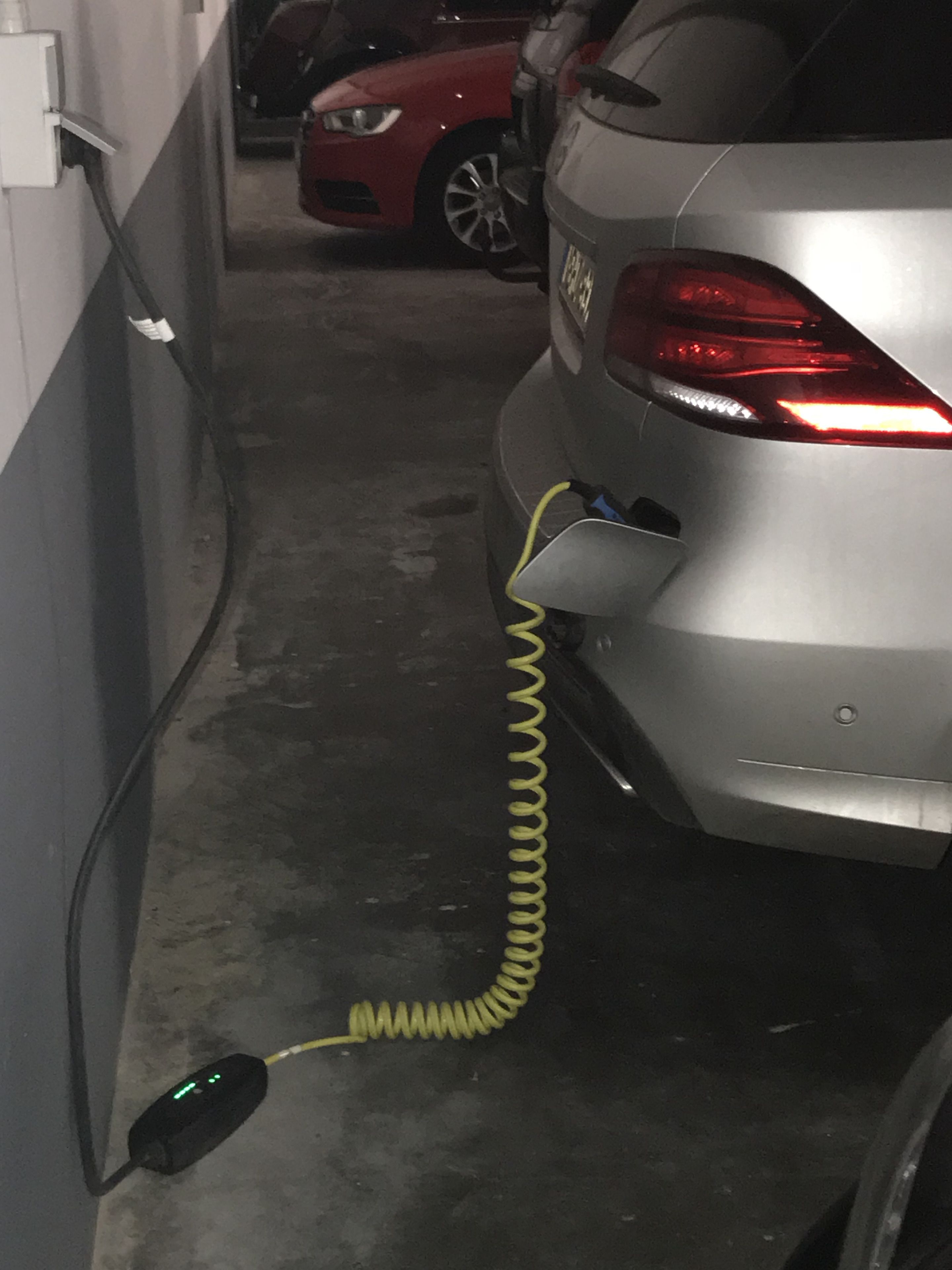 Ein Auto, das in einem schmalen Parkplatzplatz geparkt ist, mit einem Ladekabel, das an einer Wandsteckdose angeschlossen ist.