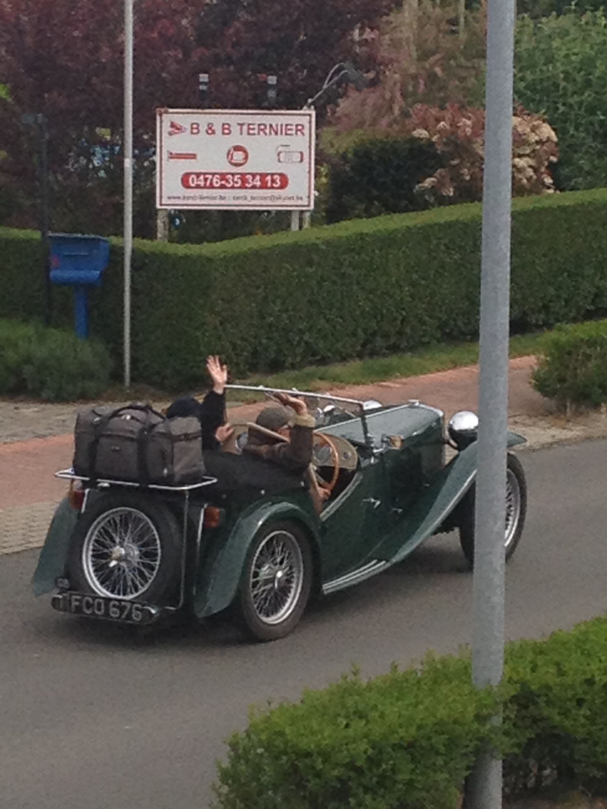 A vintage green convertible car parked on a street with a sign for B&B Ternier in the background.