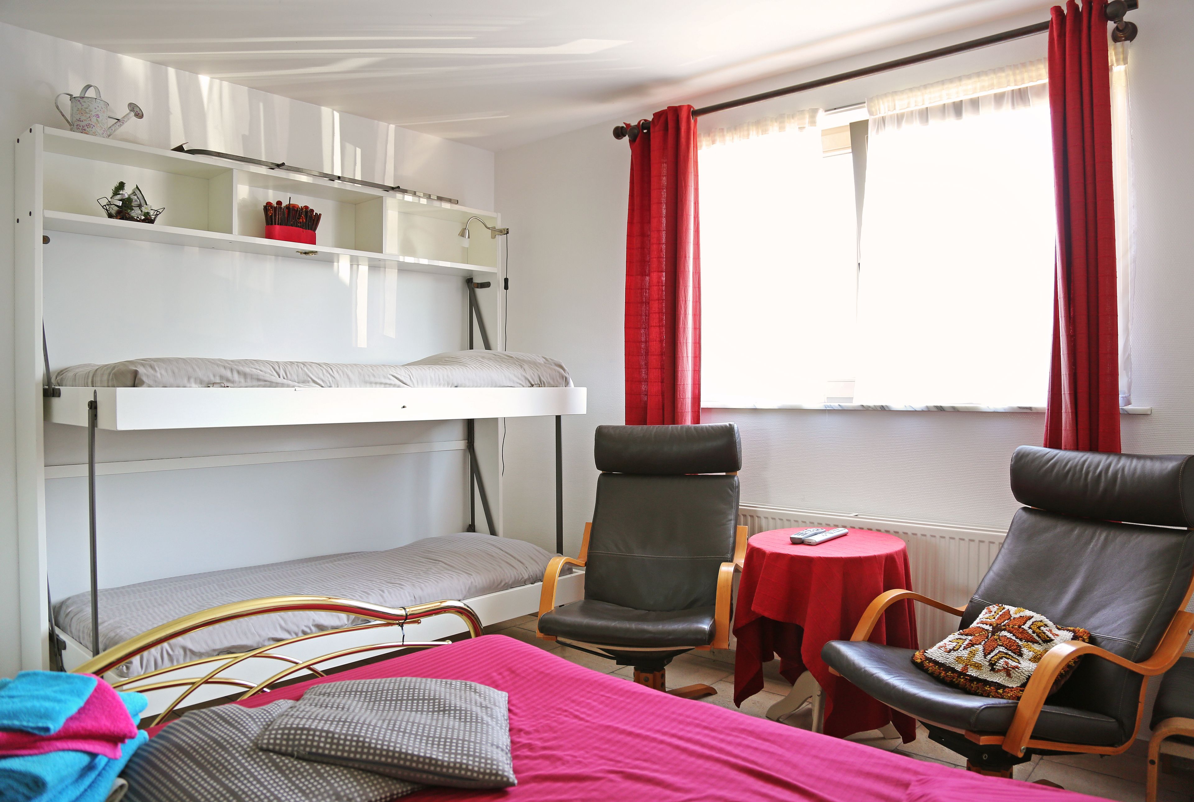A room with a bunk bed, two chairs, a small table, and a window with curtains.