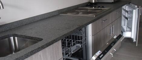 Una cocina moderna con encimera de granito, pileta de acero inoxidable y lavavajillas integrado.