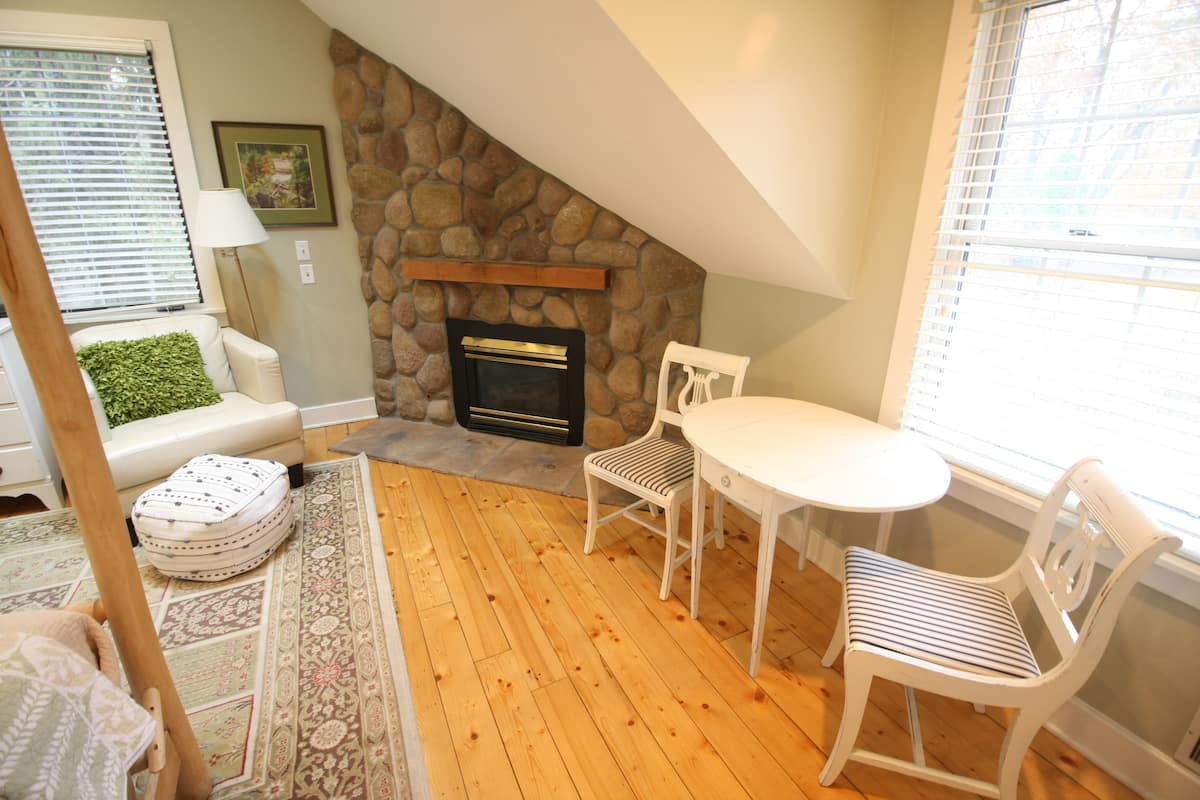 A cozy living room with a stone fireplace, a white table, and a comfortable chair.