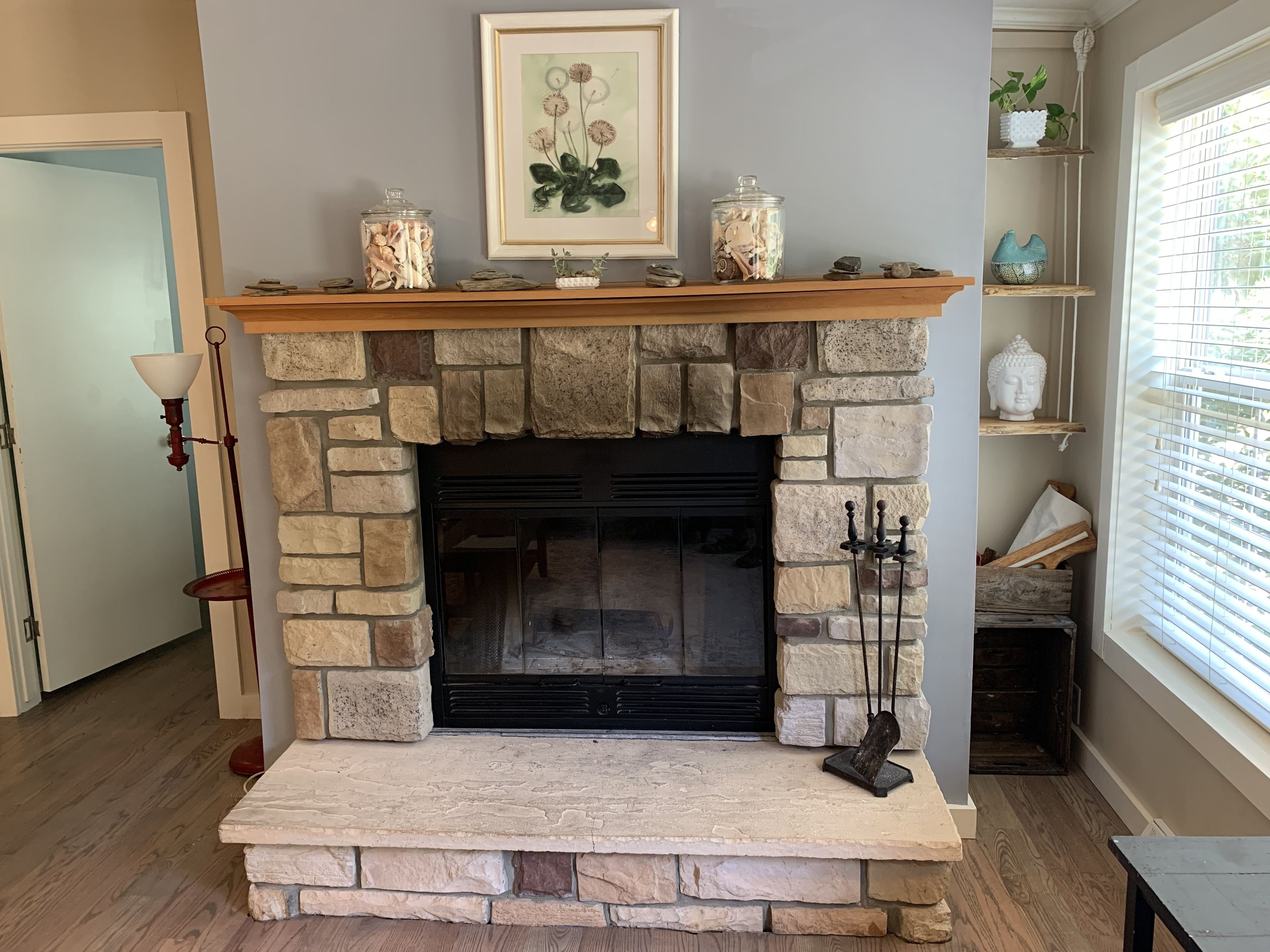 A stone fireplace with a mantel shelf, a framed botanical print above it, and a Buddha statue on the right.