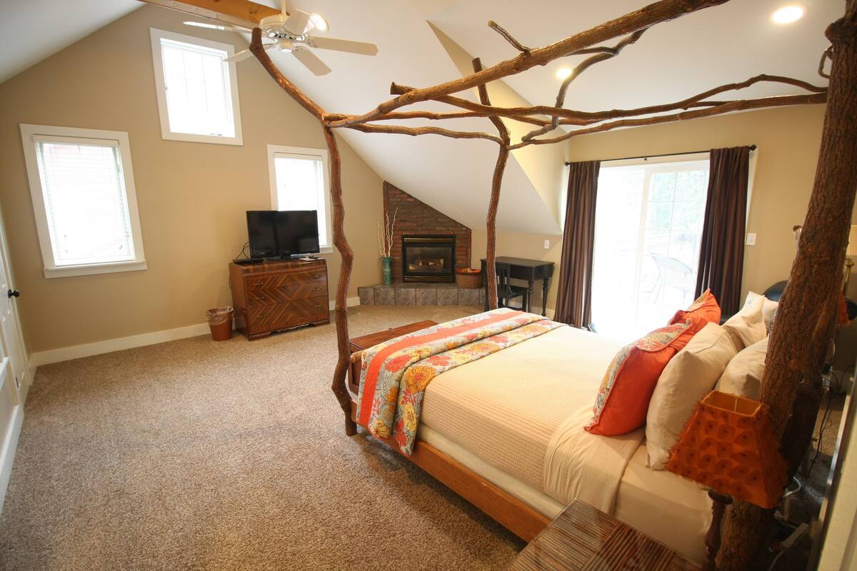 A bedroom with a sloped ceiling, a bed with a canopy, a fireplace, and a television on a dresser.