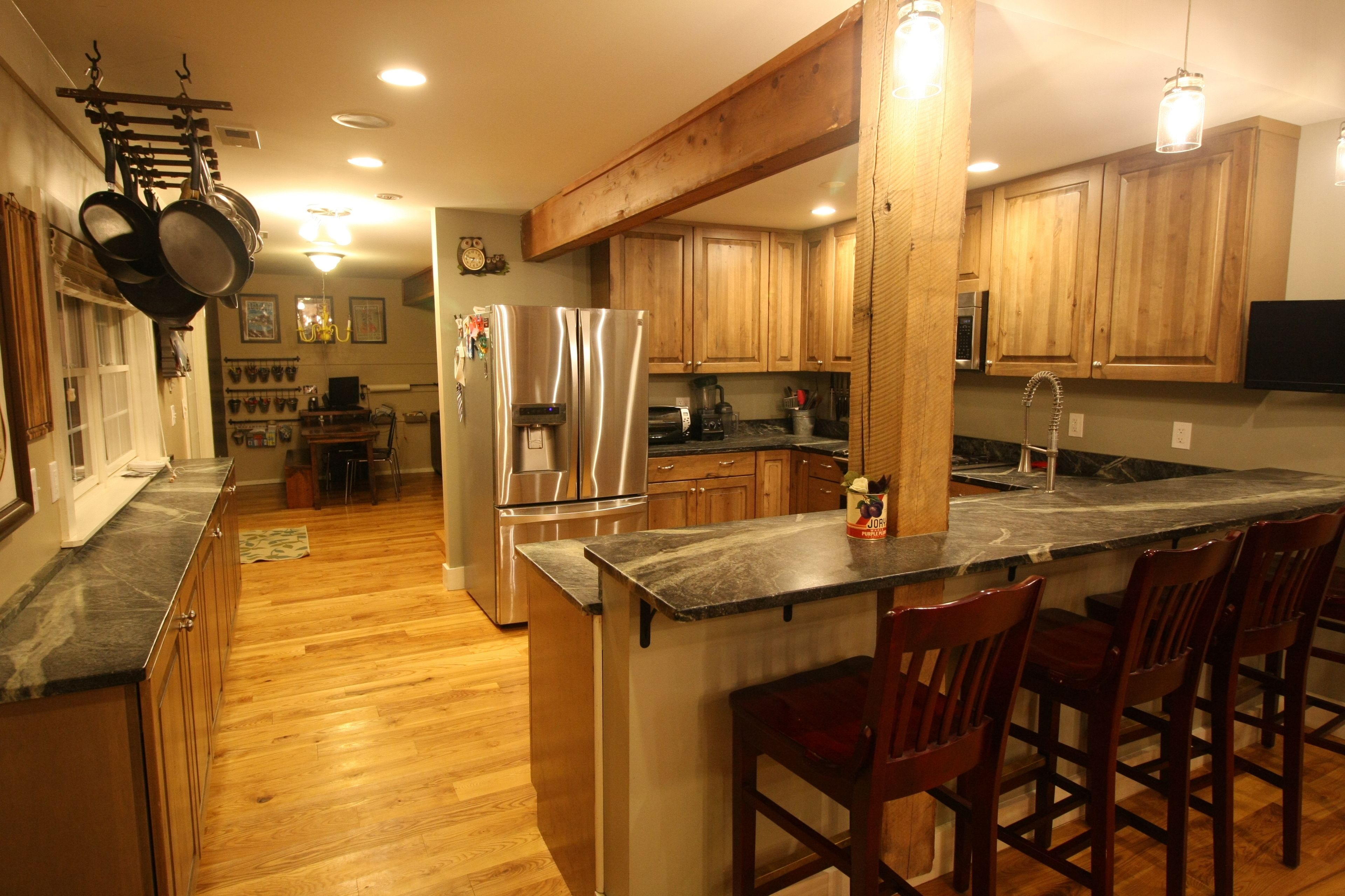A kitchen with wooden cabinets, a stainless steel refrigerator, and a marble countertop.