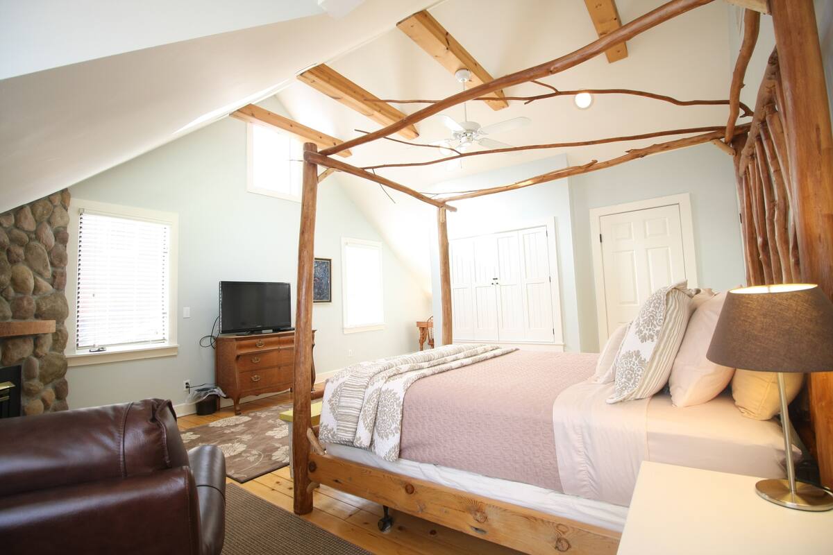 A bedroom with a four-poster bed, a stone wall, a television, and a fireplace.