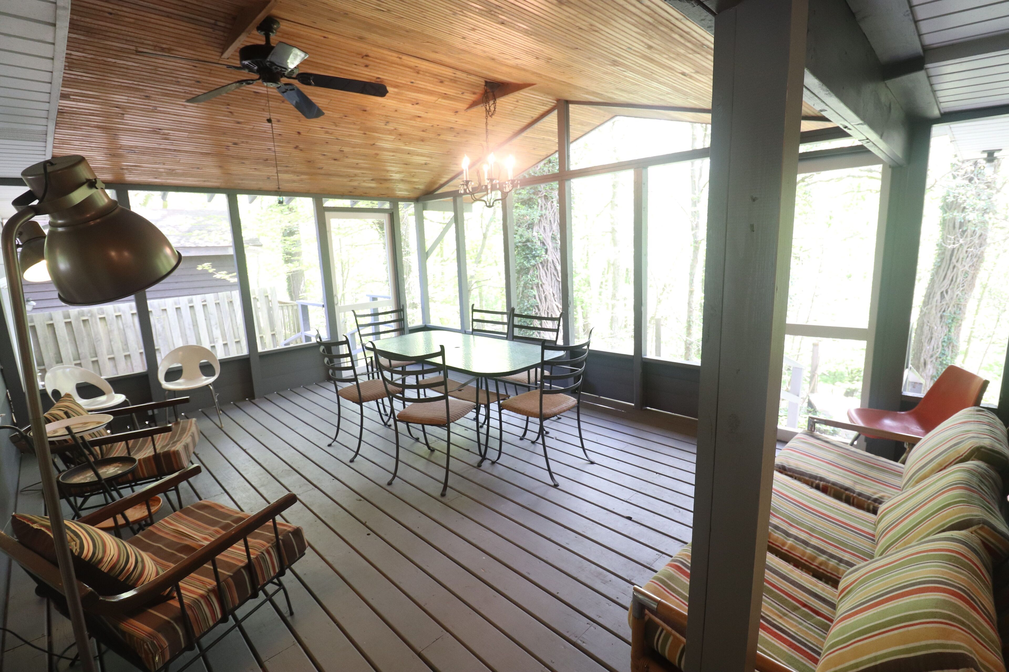 A covered outdoor seating area with a table and chairs, a ceiling fan, and a view of the outdoors.