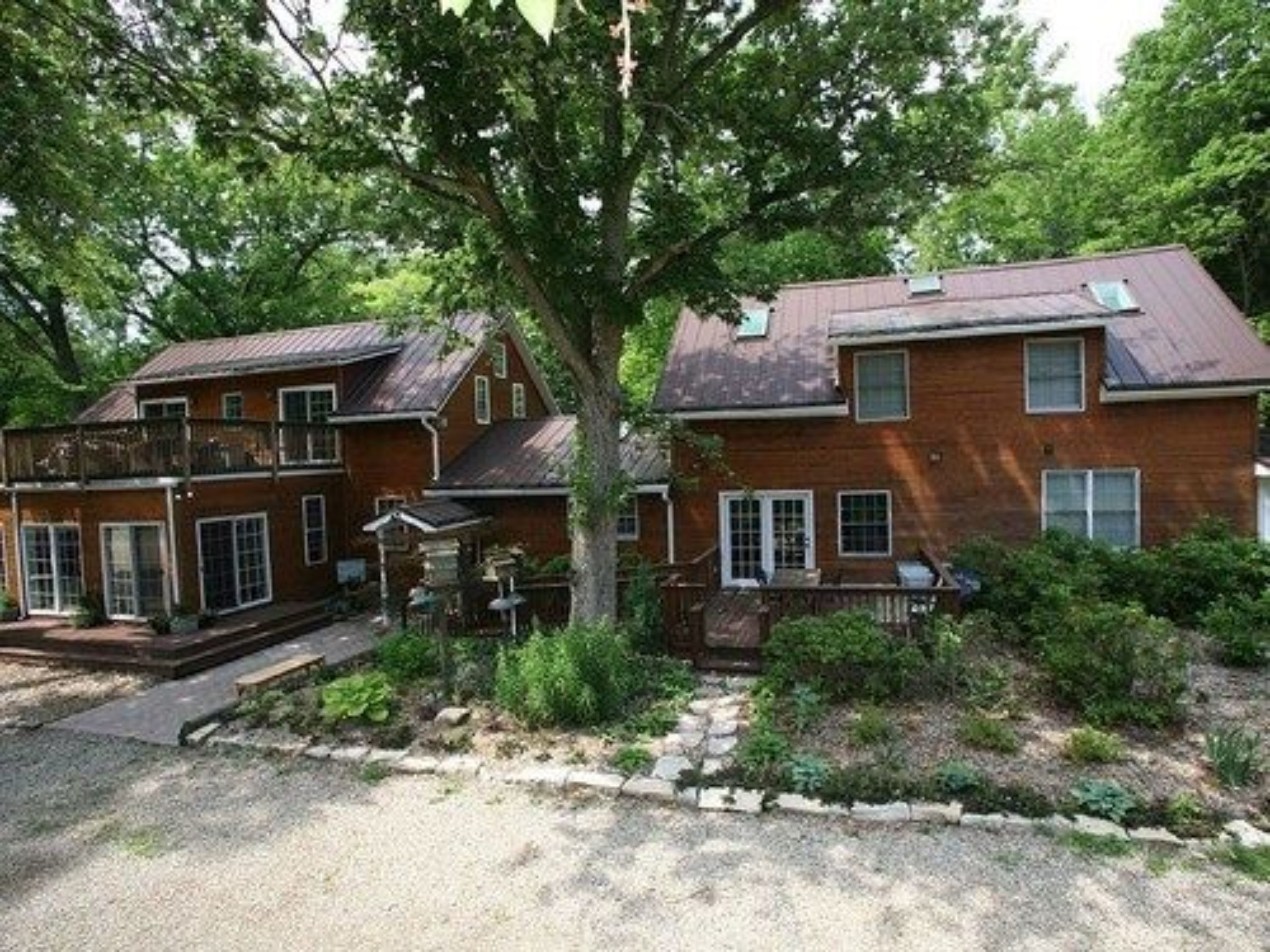 A two-story brick house with a front porch, a covered patio, and a gravel driveway.