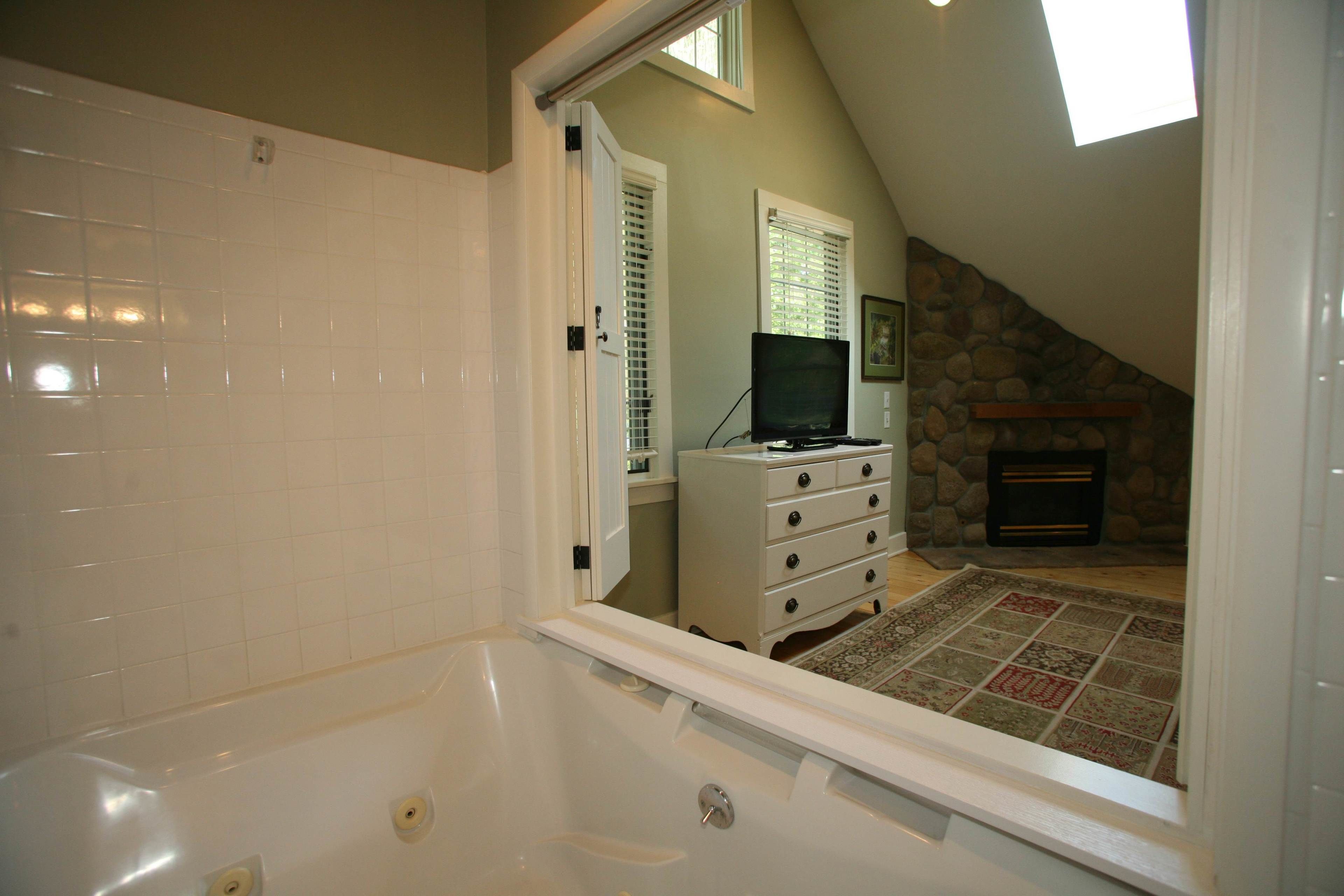 A bathroom with a bathtub, a white dresser, a television, and a stone fireplace.