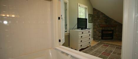 A bathroom with a bathtub, a white dresser, a television, and a stone fireplace.