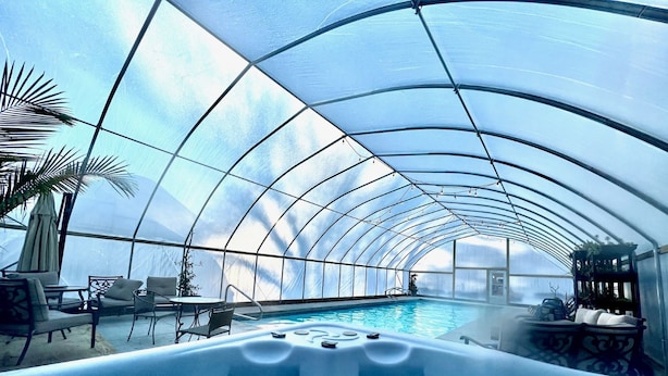 An indoor swimming pool with a glass ceiling, surrounded by lounge chairs and a hot tub. - Goldberry Woods (Union Pier)