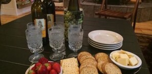 Una mesa con botellas de vino, copas, fresas, galletas y un bol de queso.