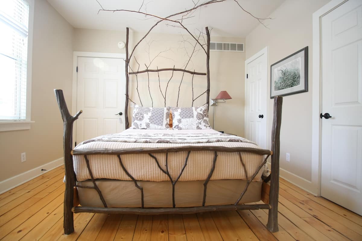 A bed with a unique branch headboard, a window with blinds, and a framed picture on the wall.