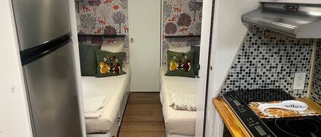 A compact RV interior with two sleeping areas, a kitchenette, and a bathroom.