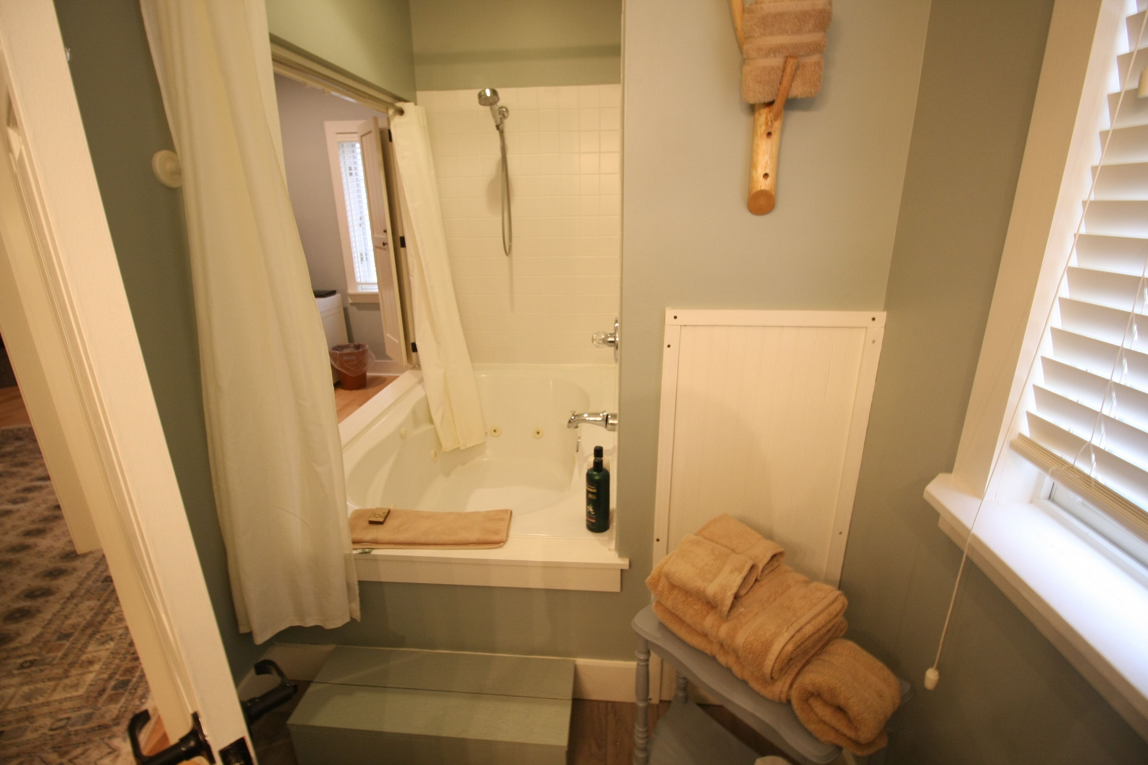 A bathroom with a bathtub, a shower, and a window with blinds.