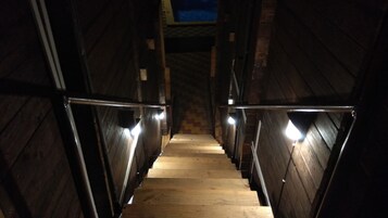 Una escalera de madera con barandillas metálicas y luces en la parte superior, que conduce a un nivel superior.