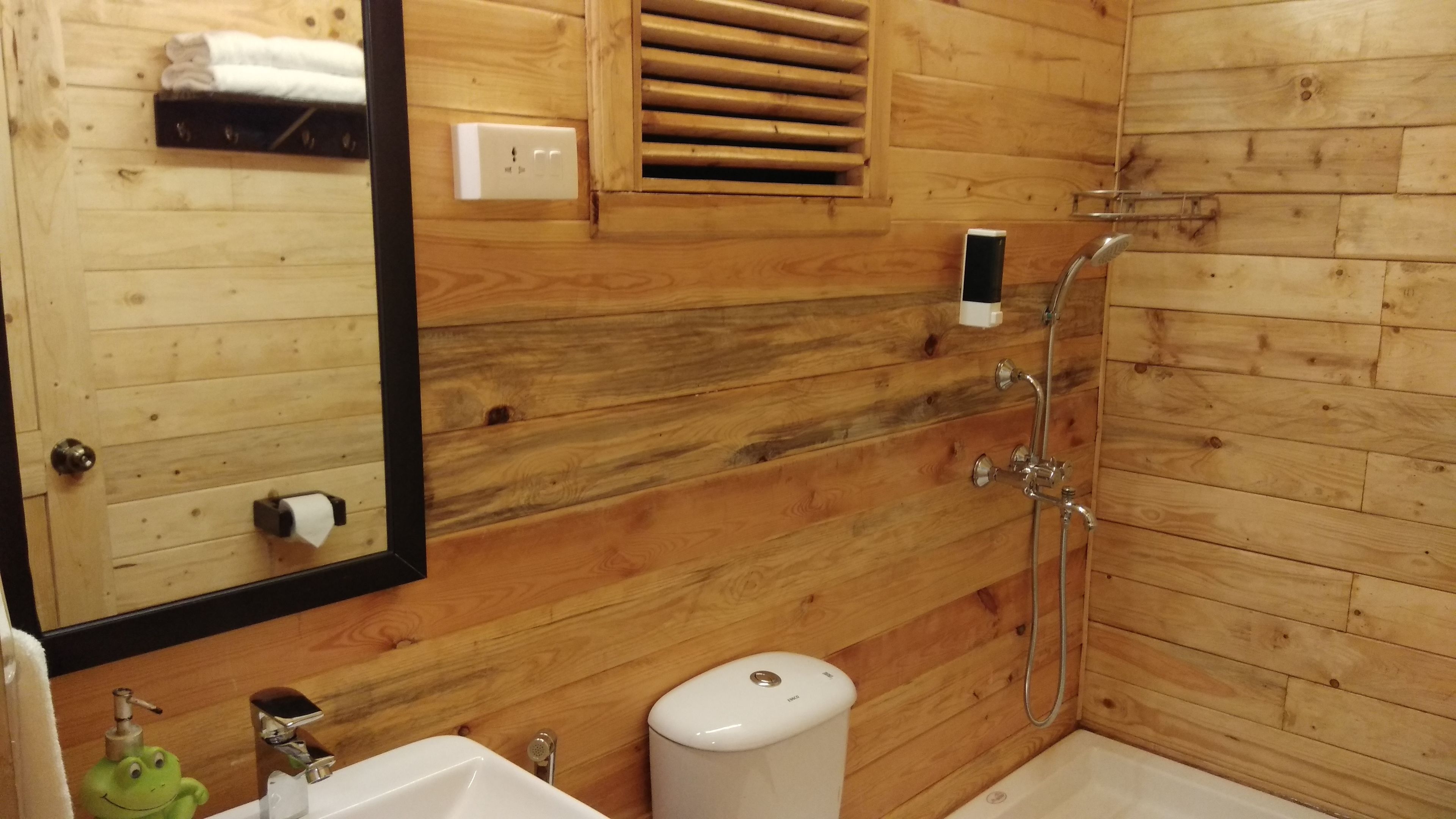A wooden-paneled bathroom with a sink, mirror, towel rack, and shower.