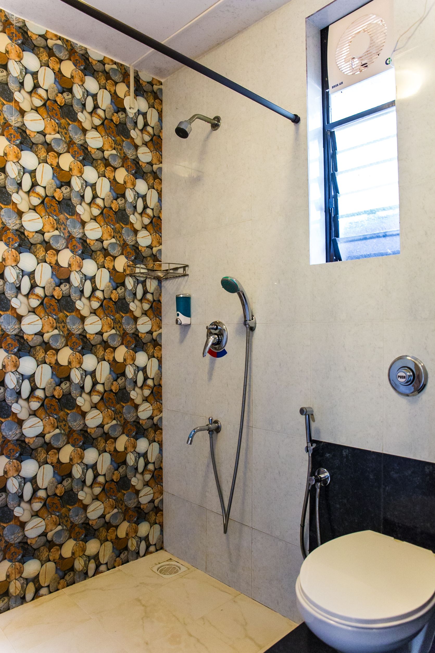 A bathroom with a pebble wall, a shower, a toilet, and a window.