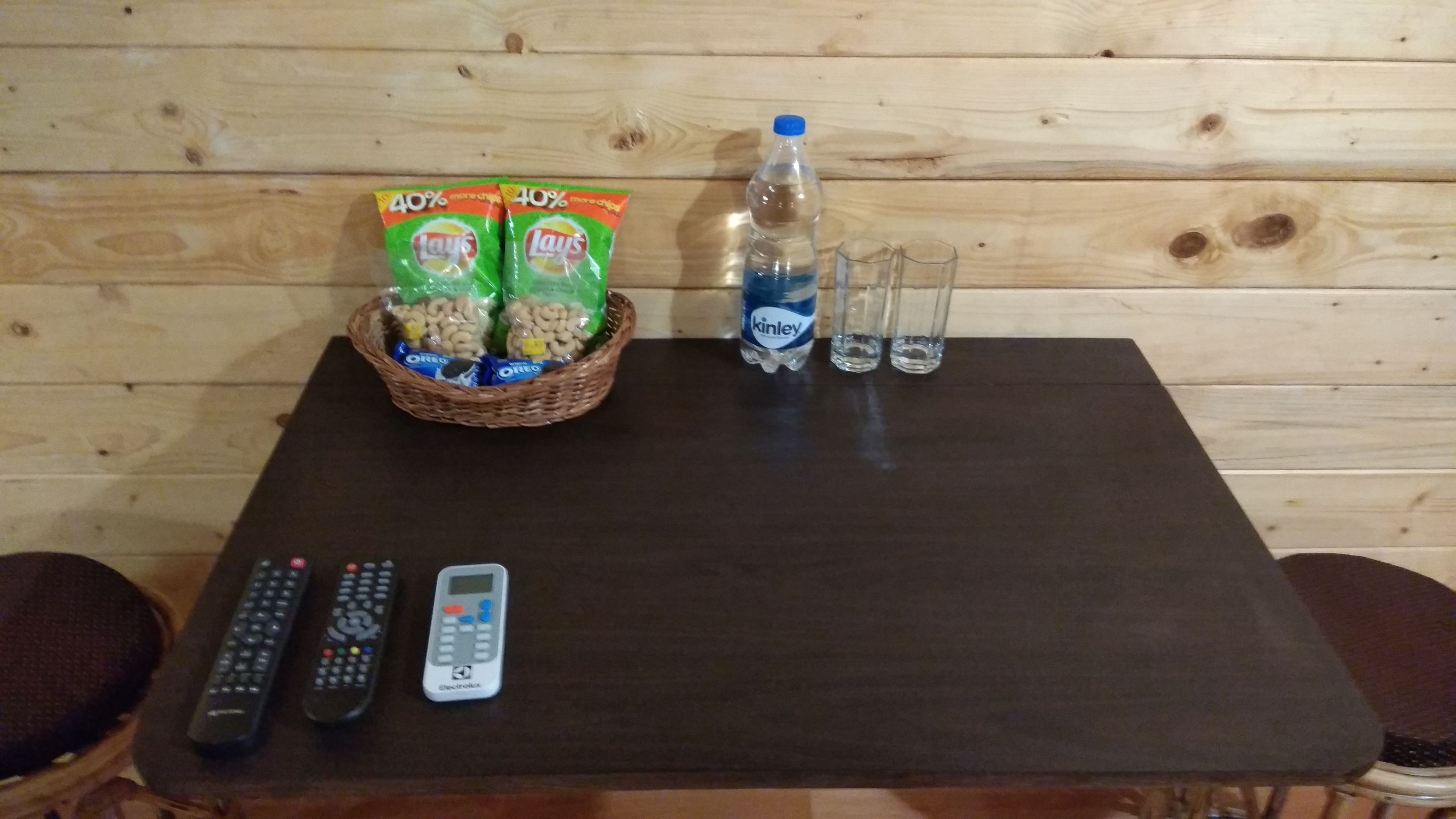 A wooden table with snacks, a bottle of water, glasses, and remote controls.