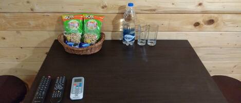 Une table en bois avec des collations, une bouteille d’eau, des verres et des télécommandes.