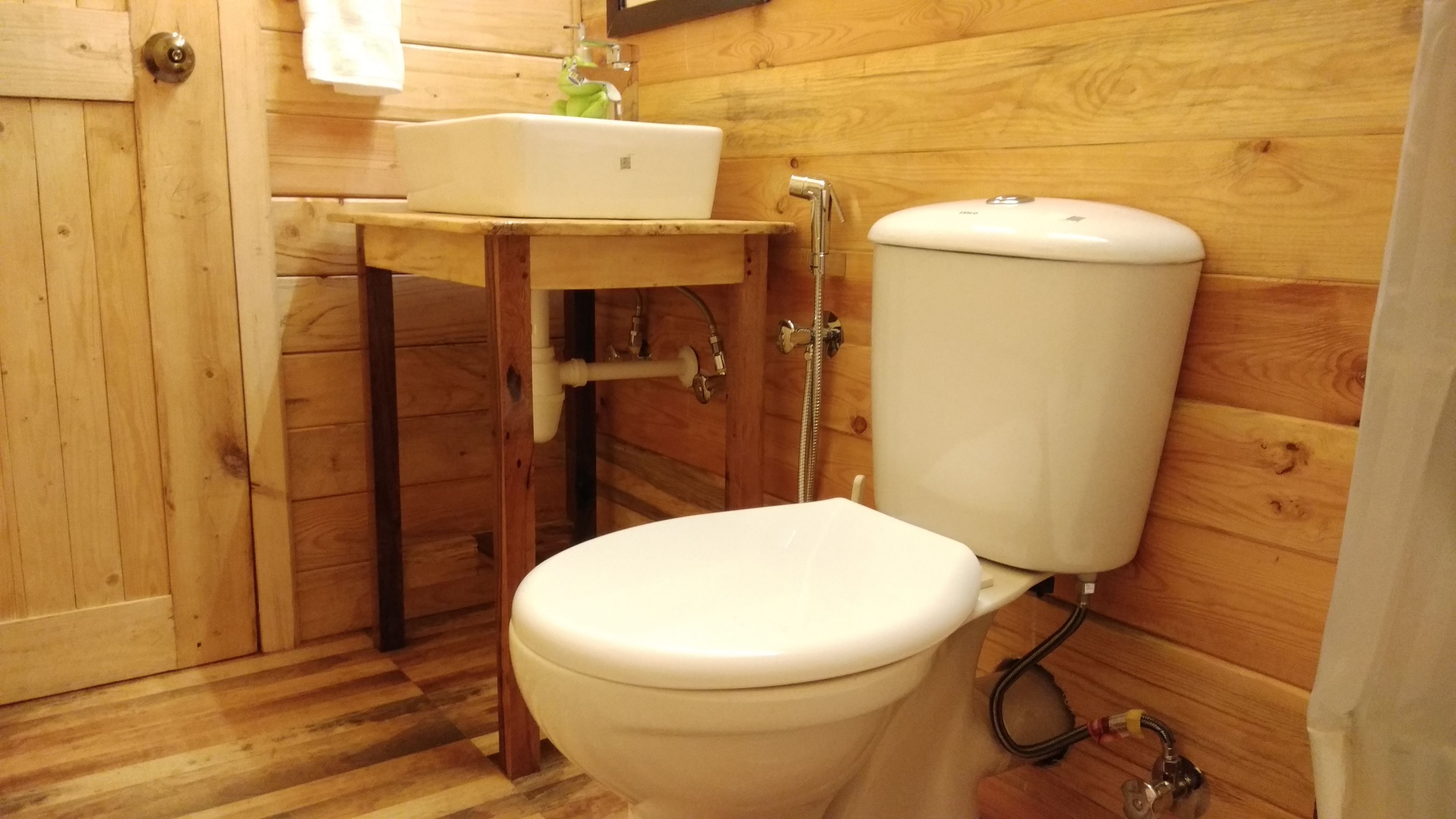A compact wooden bathroom with a toilet, a sink, and a shower.