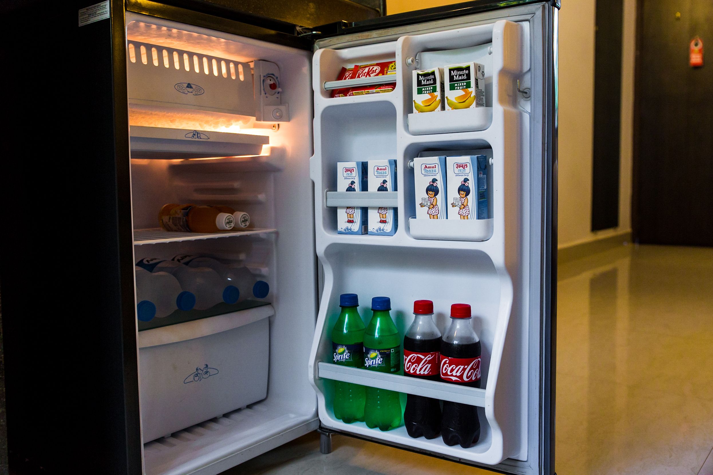 An open refrigerator with shelves containing beverages, including Sprite, Coca-Cola, and Minute Maid juice cartons.