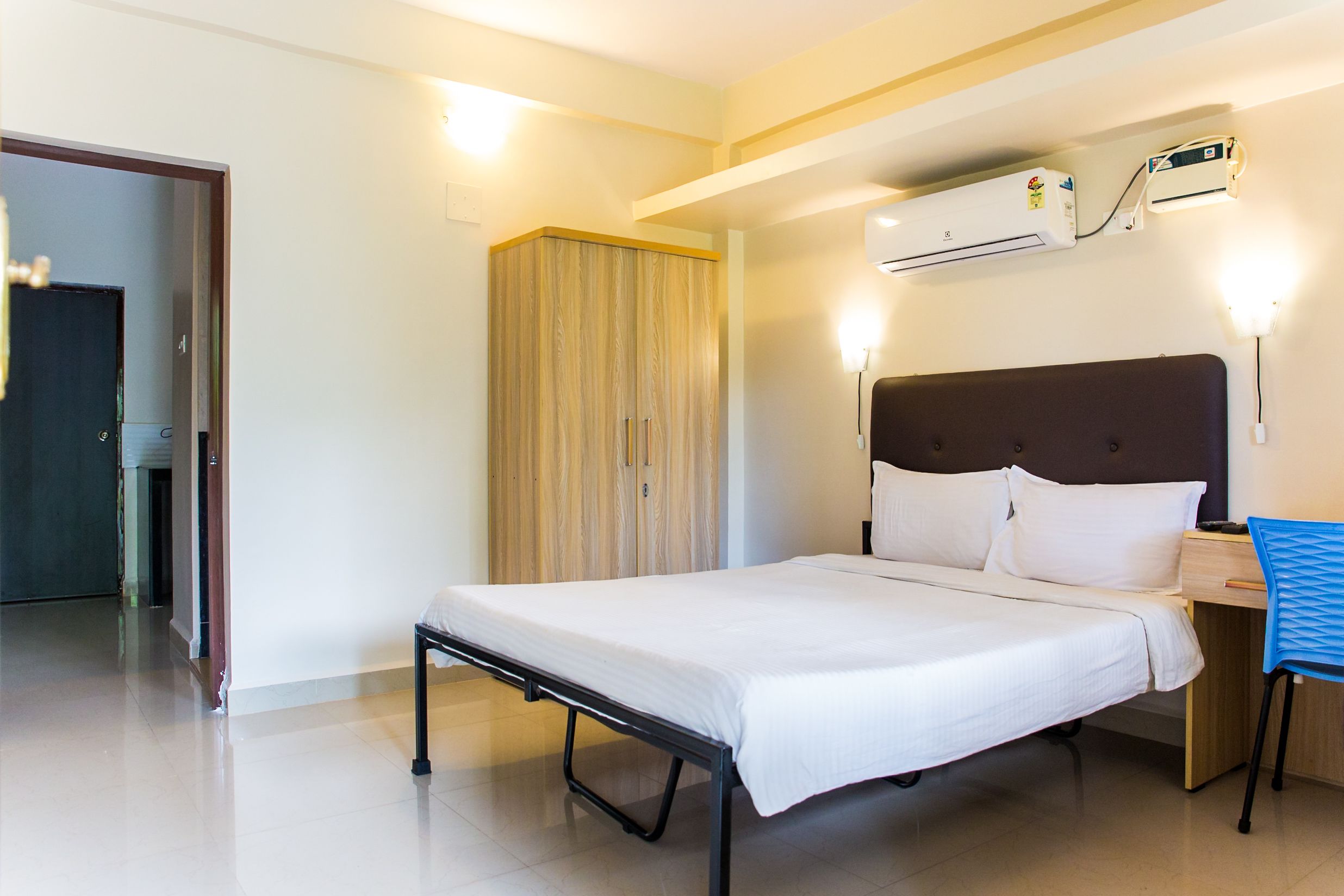 A hotel room with a bed, a desk, a chair, an air conditioning unit, and a wardrobe.
