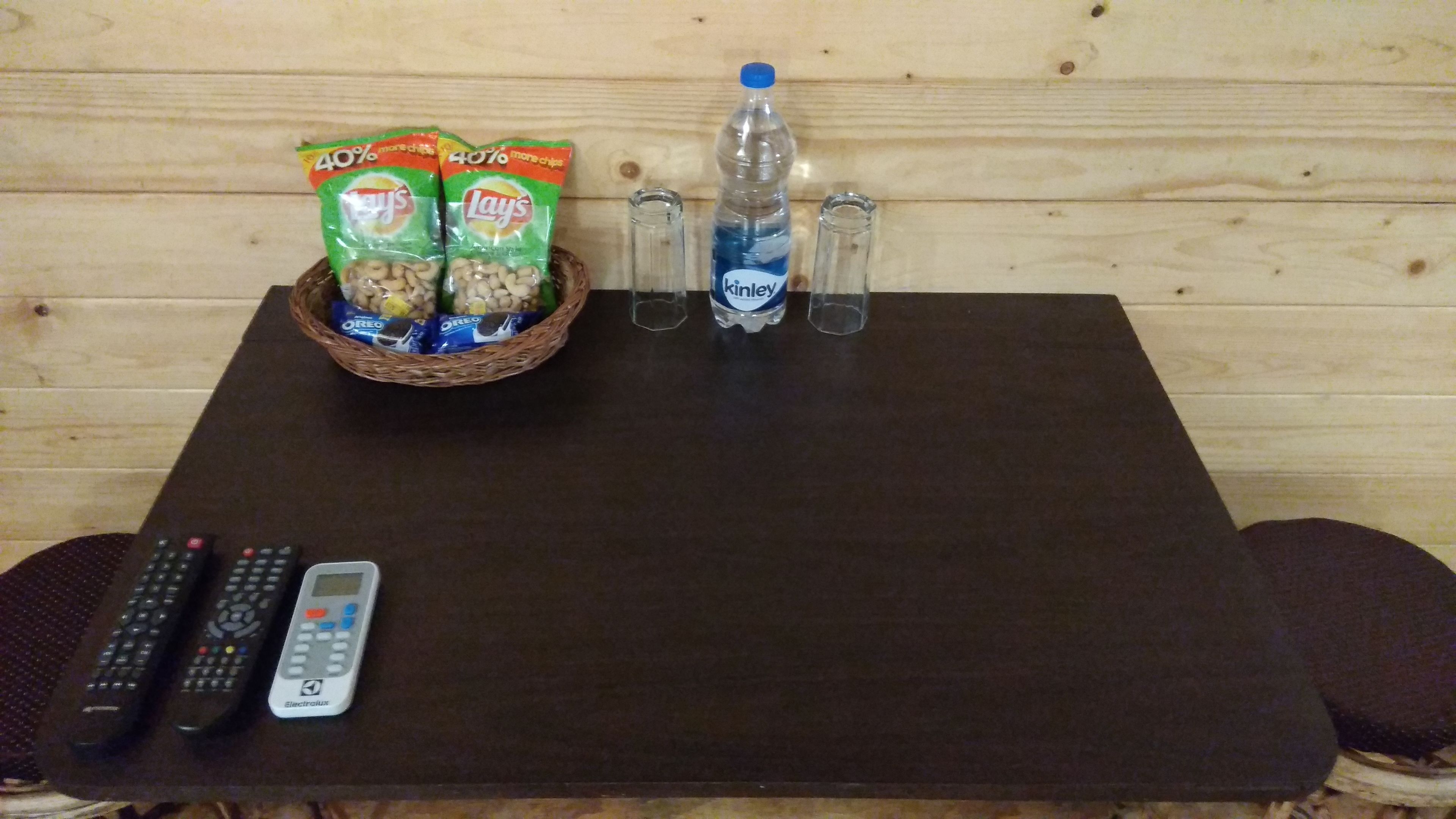 A wooden table with snacks, a bottle, and remote controls.