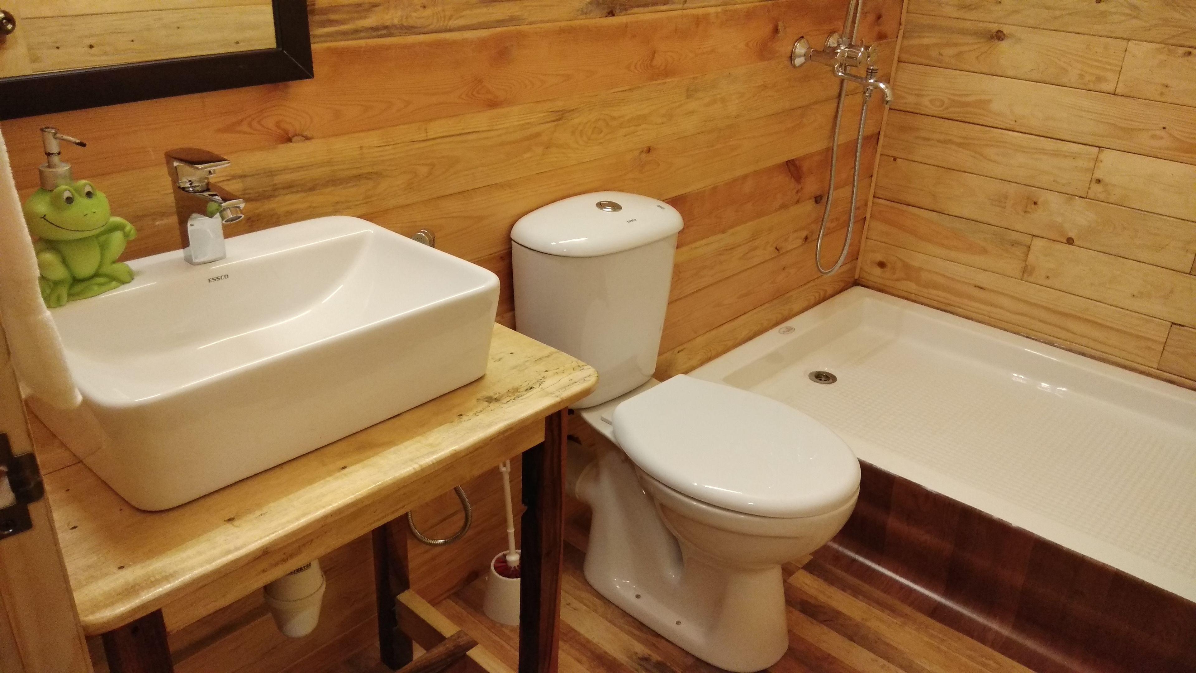 Une salle de bain aux murs lambrissés, avec un lavabo, des toilettes et une baignoire, le tout de couleur blanche.