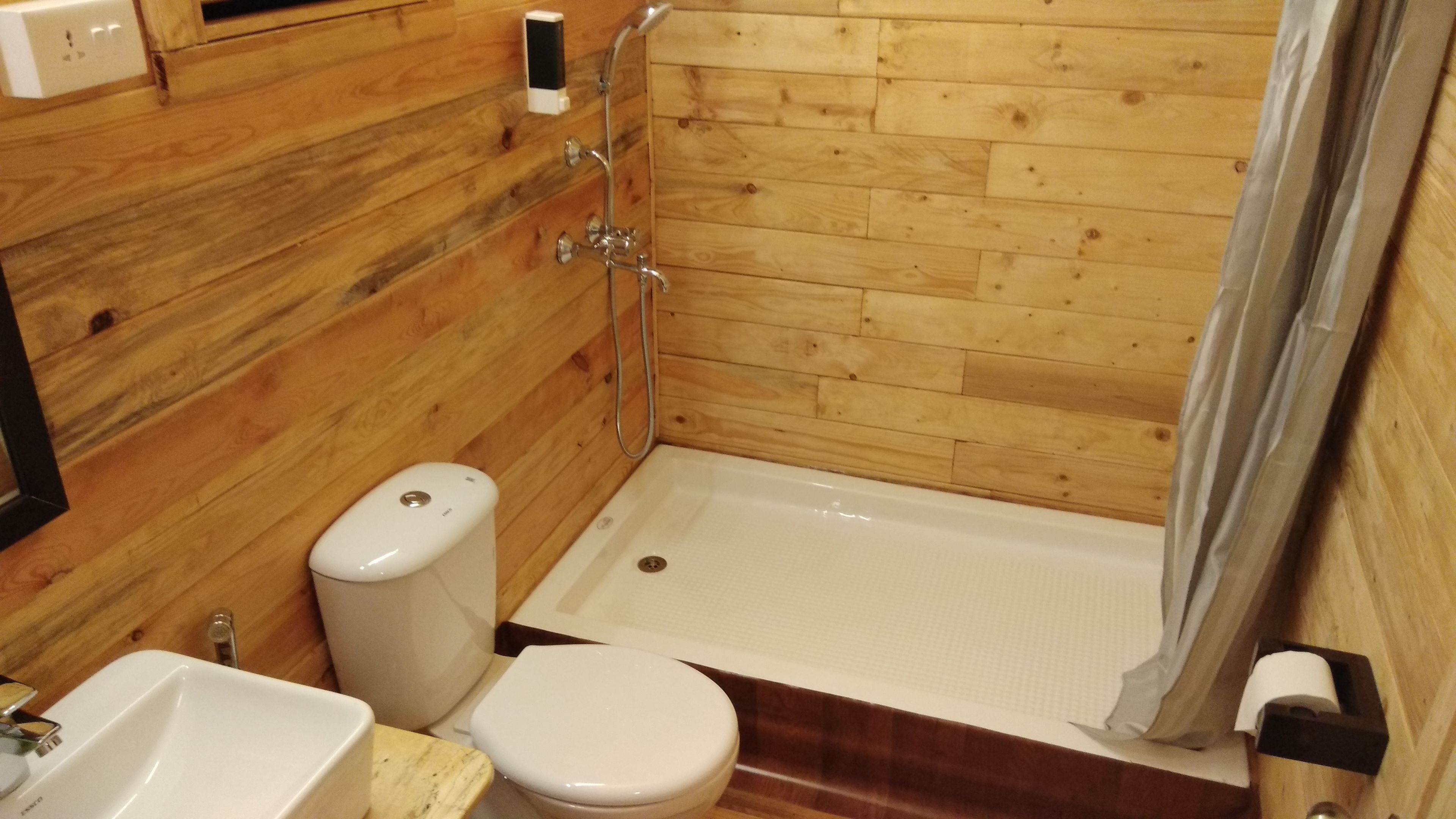 A bathroom with a wooden wall, a white bathtub, a toilet, and a sink.