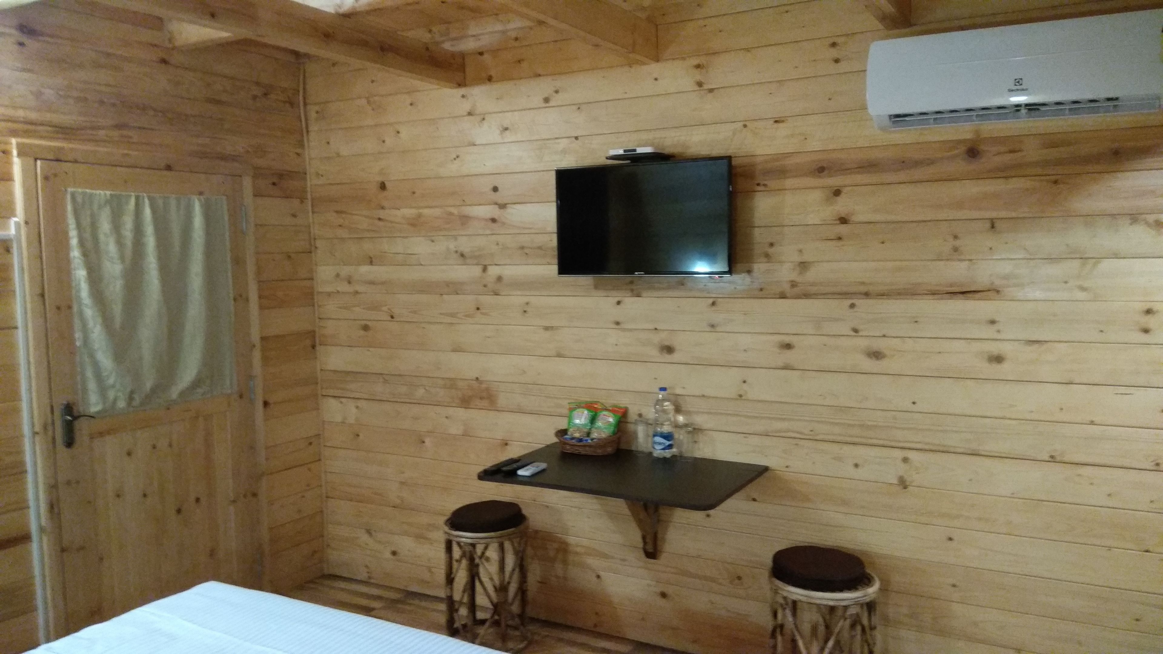 Ein Zimmer in einer Holzhütte mit einem an der Wand befestigten Fernseher, einem kleinen Tisch mit Snacks und zwei Hocker.