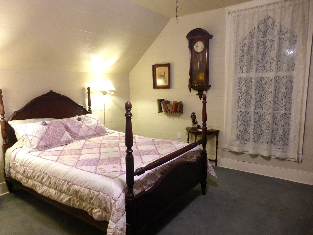 Un dormitorio con cama con dosel, un reloj de pared, un cuadro enmarco y una ventana con cortinas estampadas.