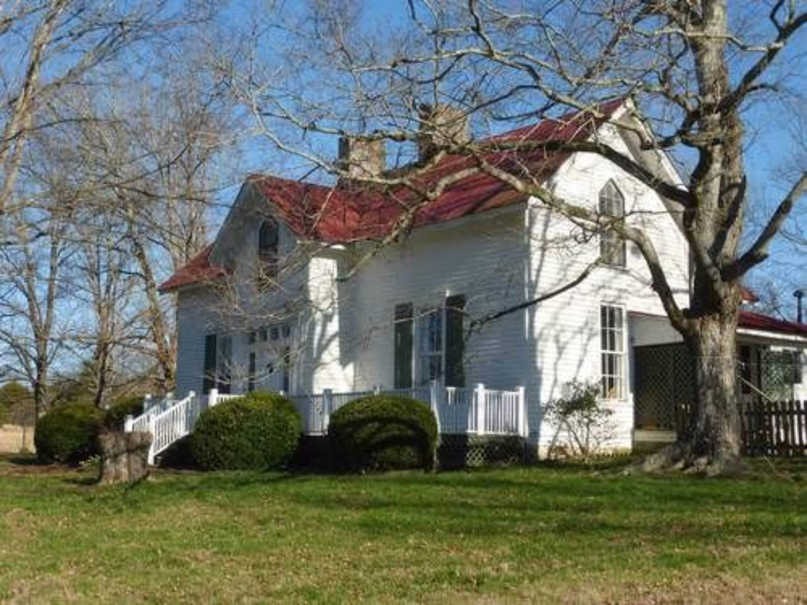 A white house with a red roof, a porch, and a small front yard.