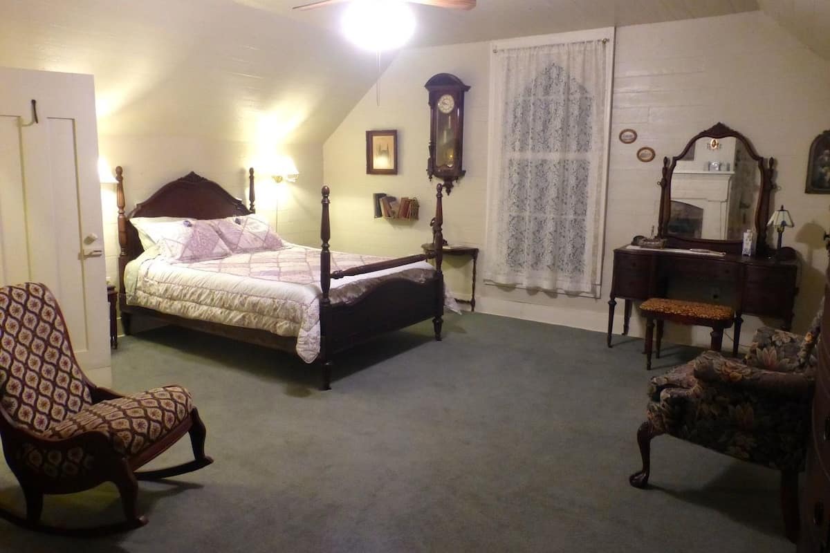 A bedroom with a four-poster bed, a chair, a dresser, a mirror, and a ceiling fan.