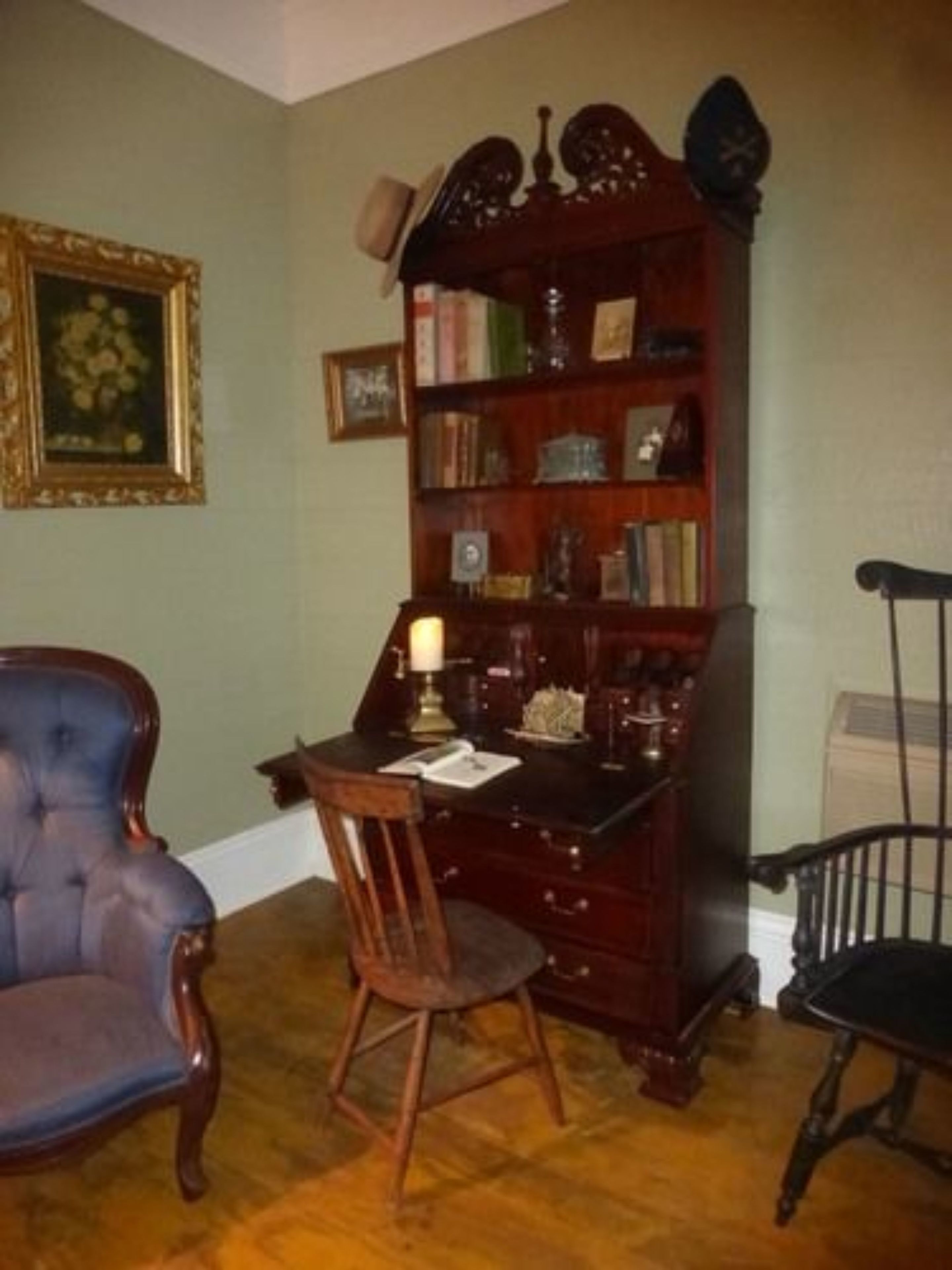 A room with a wooden desk, a blue chair, a wooden chair, and a bookshelf.