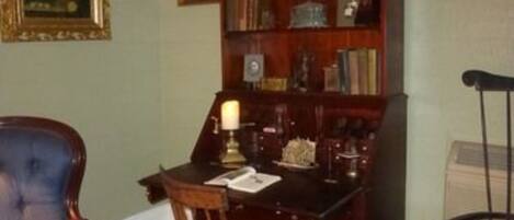 A room with a wooden desk, a blue chair, a wooden chair, and a bookshelf.
