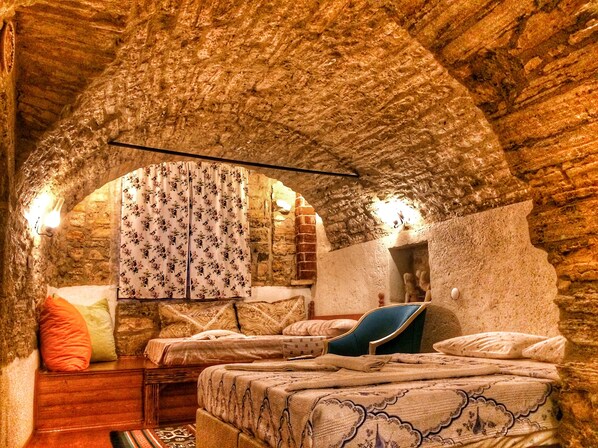 A rustic room with exposed brick walls, a wooden bed, a blue chair, and a patterned curtain. - Parmis Boutique House (Cesme)