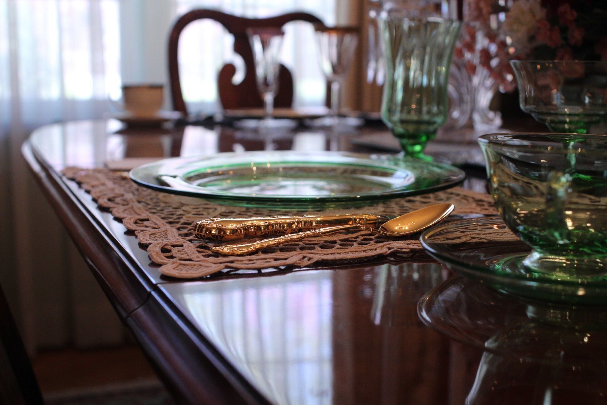 A dining table with a lace table runner, green glassware, and a golden spoon.