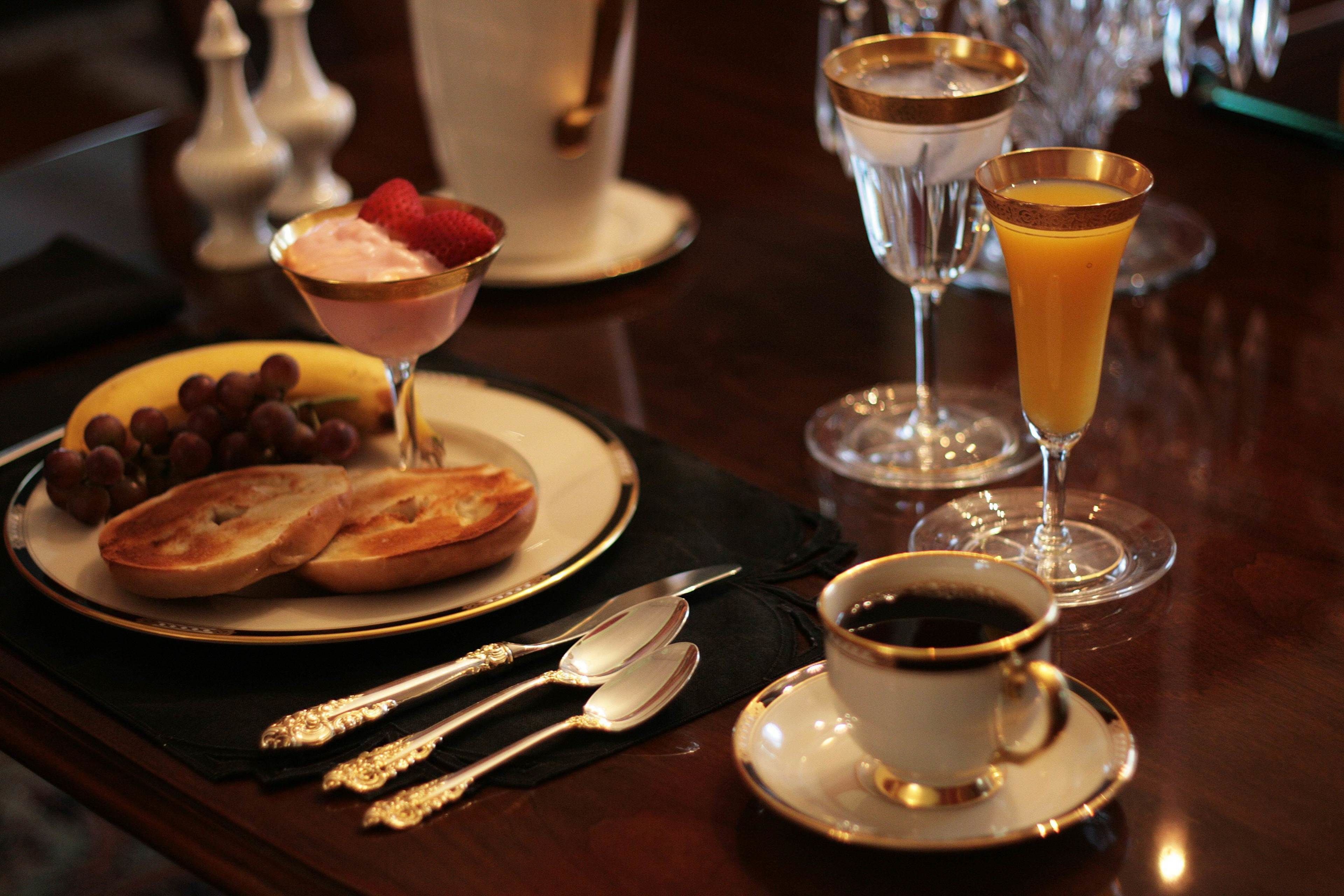 A table set with a plate of bread, grapes, and a dessert with a strawberry, two glasses of orange juice, and a cup of coffee.