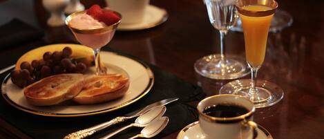 A table set with a plate of bread, grapes, and a dessert with a strawberry, two glasses of orange juice, and a cup of coffee.