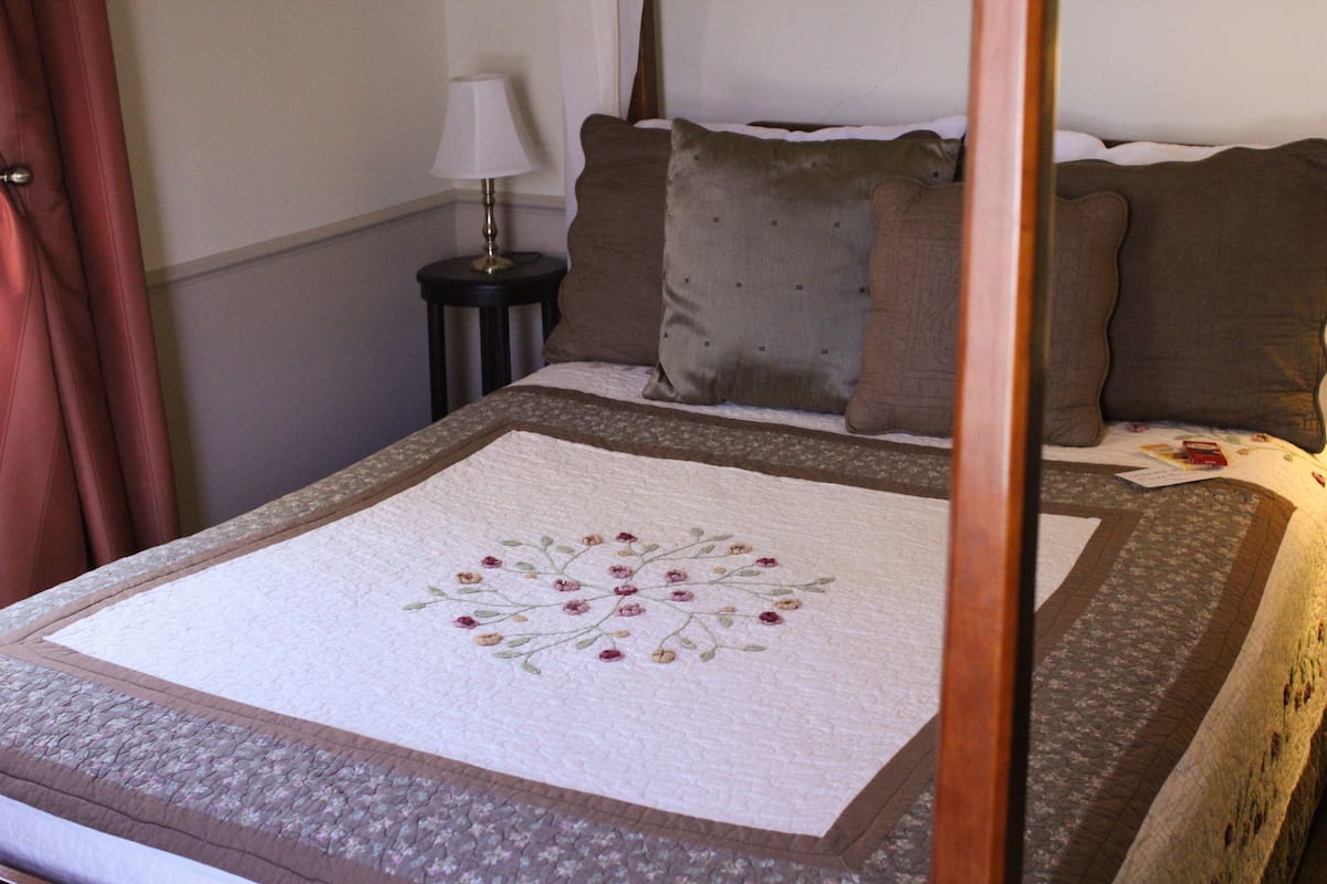 A neatly made bed with a floral quilt, a bedside lamp, and a nightstand with a lamp.