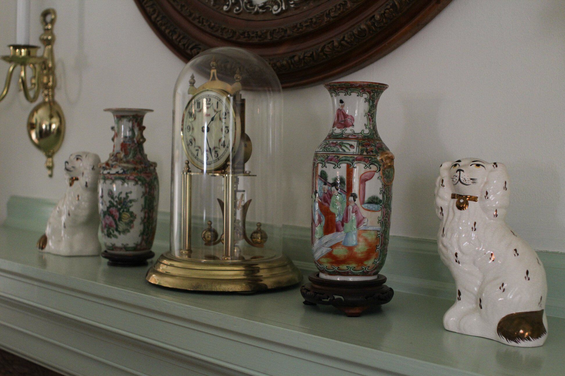 A collection of decorative items on a shelf, including a clock, a vase with a figure, and a ceramic dog.