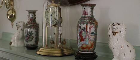 A collection of decorative items on a shelf, including a clock, a vase with a figure, and a ceramic dog.