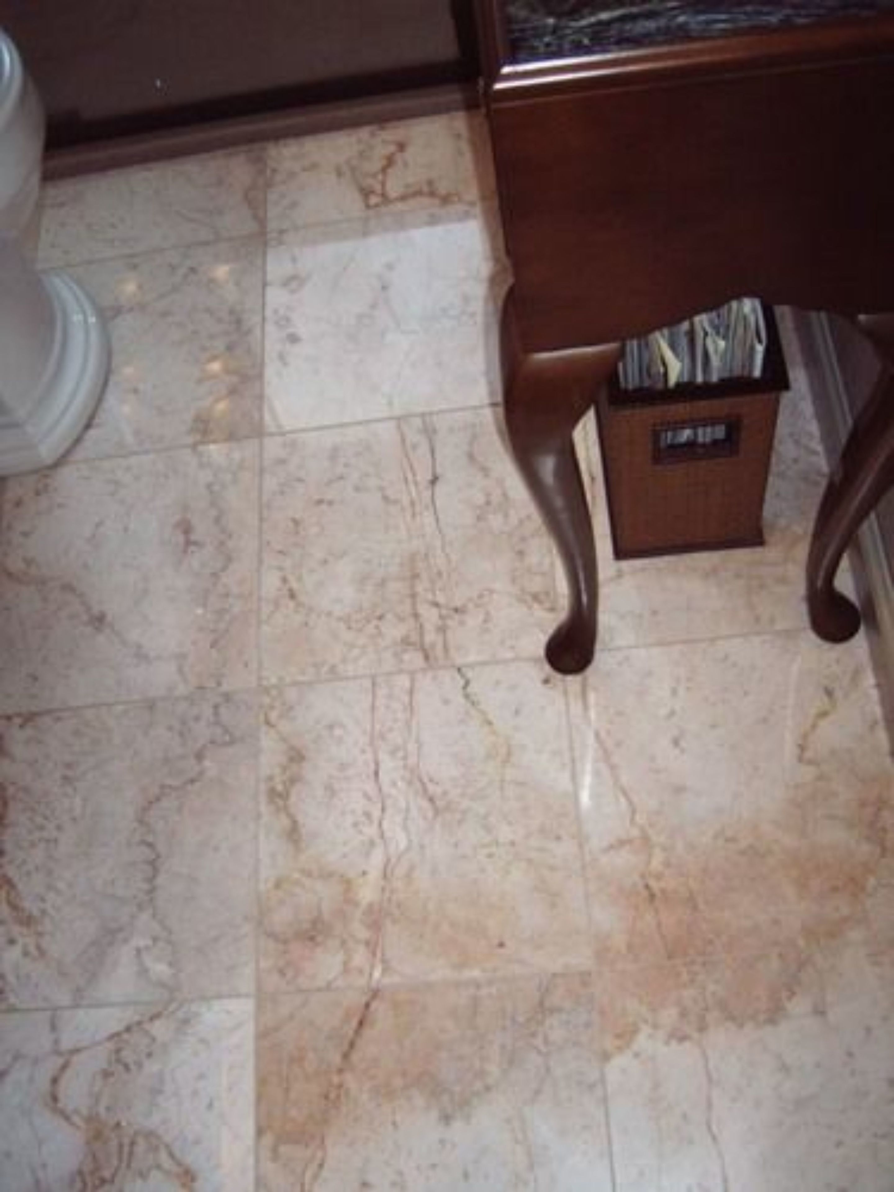 Un baño con piso de mármol, un mueble de madera y un cesto de basura.