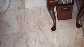 Un baño con piso de mármol, un mueble de madera y un cesto de basura.